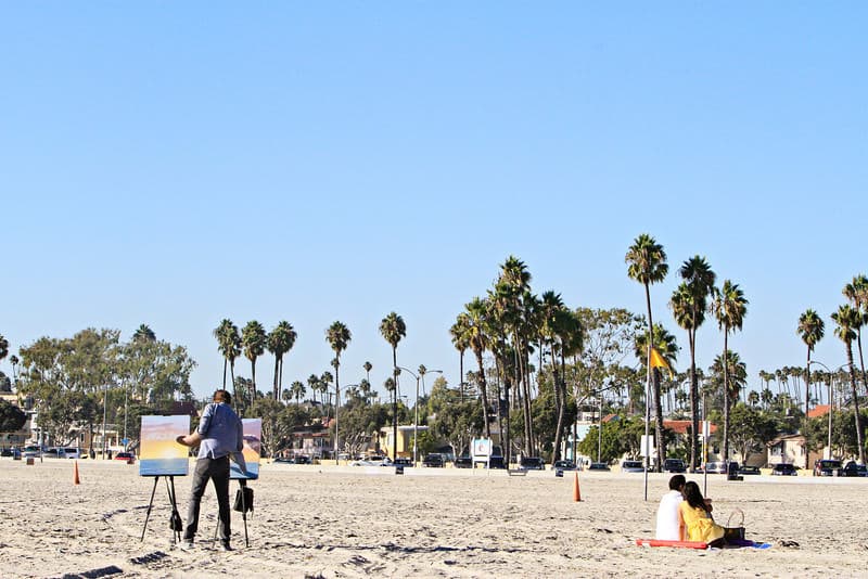 Sameer at the beach with Nisha and a painter behind them